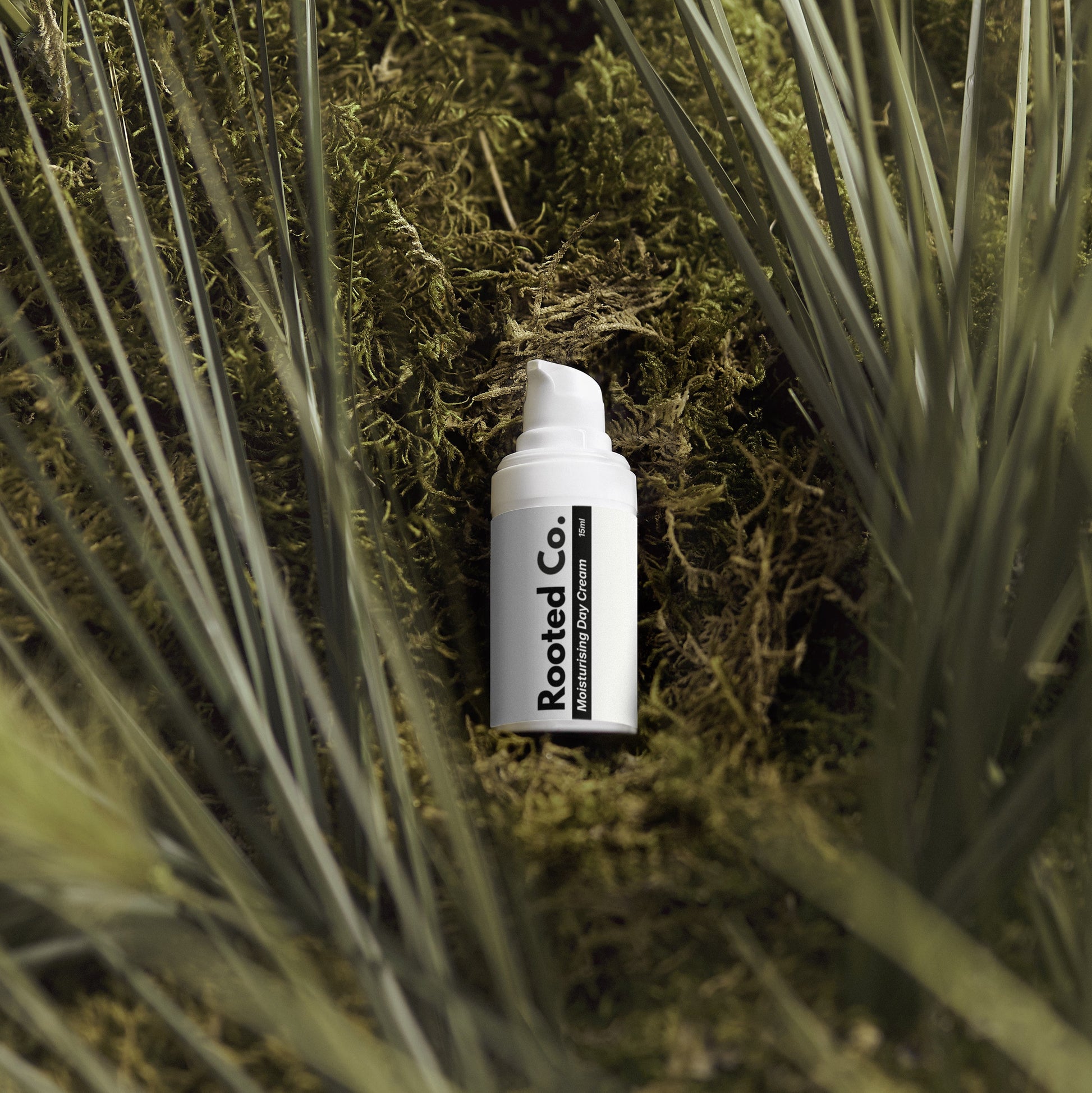 White bottle labeled 'Rooted Co.' on a bed of moss and grass